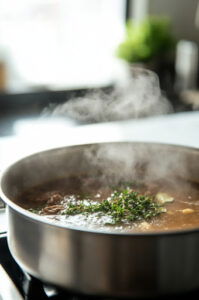 This image shows a pot of simmering onions, with bay leaves and sprigs of thyme being added, along with a pour of rich, flavorful stock.