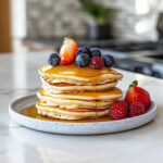 this image shows pancakes ready to be served with berries and syrup