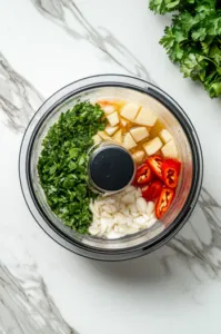 This image shows a small food processor blending fresh coriander, garlic, ginger, soy sauce, olive oil, and water to create a smooth ginger soy sauce.