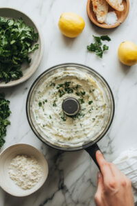 This image shows a blender in action, combining cottage cheese, pickled jalapenos, sun-dried tomatoes, scallions, and garlic chives into a smooth, creamy dip.