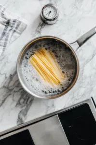 This image shows gluten-free spaghetti boiling in a pot of water, with steam rising as the pasta cooks until al dente.