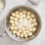 This image shows a plate of golden brown gnocchi, beautifully coated in a rich brown butter sauce, garnished with fresh sage leaves and sprinkled with shredded Parmesan cheese.