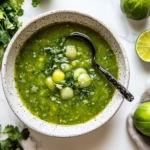 This image shows a vibrant bowl of Chipotle Green Salsa, featuring a smooth, roasted tomatillo and jalapeño blend, garnished with fresh cilantro and lime wedges, ready to be served.