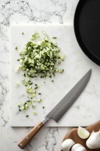 This image shows finely chopped scallions and garlic chives on a cutting board, ready to be used as a fresh topping later.