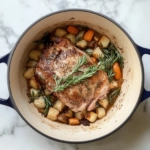 This image shows a tender, shredded cider braised pork shoulder, served with roasted baby red potatoes and honeycrisp apple slices, all bathed in a rich, golden apple cider sauce.