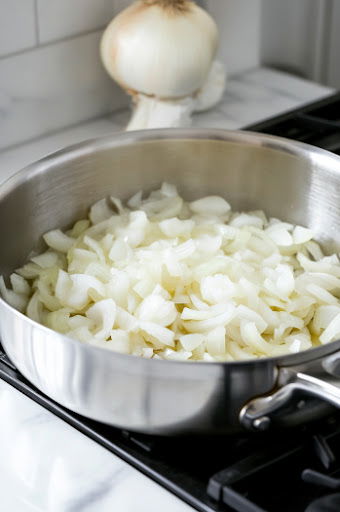 This image shows sliced onions in a pot, being tossed and coated with melted butter or oil. The onions are starting to soften as they cook.