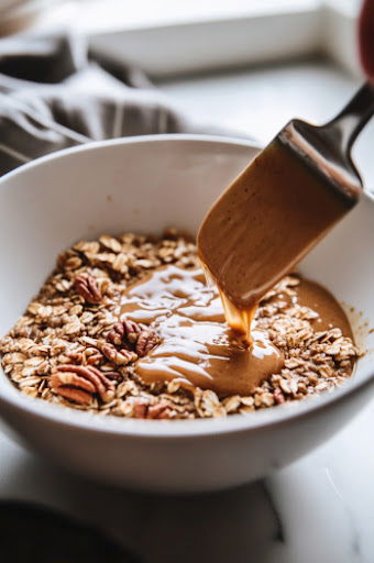 This image shows the wet ingredients being poured over the oat mixture in the large bowl, with everything being stirred until well coated.