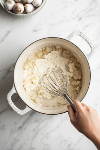 this image shows Flour being whisked into the onions and bacon drippings to form a thick base.