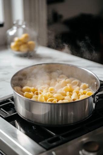 This image shows pasta being boiled in a large pot of salted water until al dente, following the package instructions.