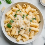 This image shows a plate of creamy rigatoni pasta topped with fresh basil and grated Parmesan, served in an elegant setting perfect for date night.