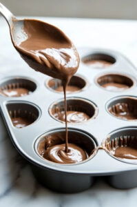 This image shows the muffin batter being poured into greased muffin tins, filling each tin halfway.