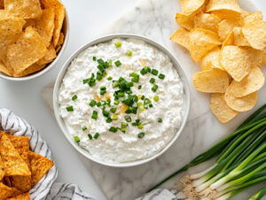 This image shows a white bowl filled with spicy cottage cheese dip, drizzled with chili oil and garnished with fresh scallions and garlic chives, ready to serve.