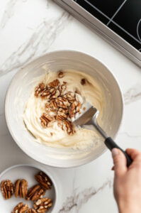 This image shows a spatula gently folding mixed nuts into the beaten egg whites, ensuring they are evenly coated.