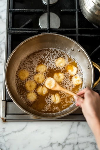 This image shows tablespoons of batter being dropped into hot oil, frying for 2-3 minutes until the fritters are golden brown