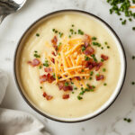 this image shows A bowl of potato soup garnished with crispy bacon, ready to be served.