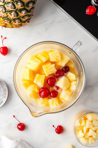 This image shows a glass of Pina Colada Sangria being garnished with fresh pineapple slices