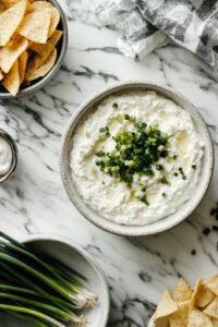 This image shows finely chopped scallions and garlic chives being sprinkled on top of the finished spicy cottage cheese dip for a fresh, colorful garnish.