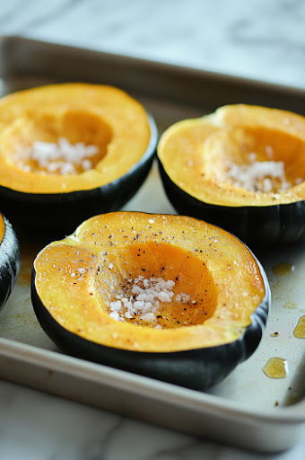 This image shows acorn squashes being cut in half, with the seeds and membranes being scooped out.