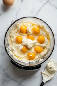 This image shows eggs and vanilla being added to the chocolate-sugar mixture and blended until smooth, creamy, and liquid.