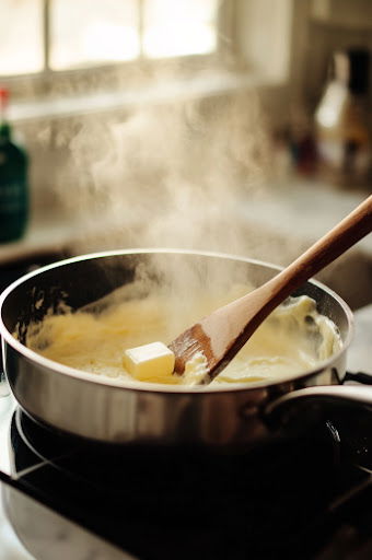 This image shows a medium saucepan on medium heat with sugar, butter, and cream being combined and stirred to make a rich vanilla cream sauce.