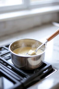 This image shows butter melting and sugar dissolving in a saucepan over gentle heat, with stirring to combine the ingredients.