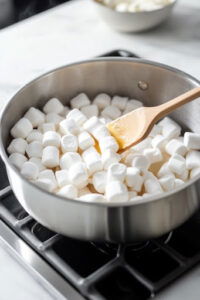 This image shows butter and marshmallows gently melting over low heat in a saucepan, stirring until fully combined and smooth.