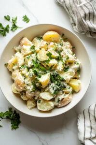 This image shows mayo, spicy mustard, salt, and pepper being mixed with the diced potatoes and grated eggs in a large bowl.