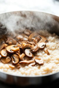 This image shows two-thirds of the sautéed mushrooms being mixed into the pan with the final portion of broth.