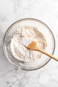 This image shows a separate bowl with flour, baking soda, cinnamon, ginger, cloves, and salt being whisked together to combine the dry ingredients.