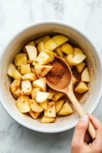 This image shows a bowl of sugar, cinnamon, cloves, and salt being poured over the apples in the slow cooker.