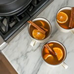 This image shows the final mulled cider served in a white mug, garnished with a cinnamon stick and an orange slice on top, ready for drinking.