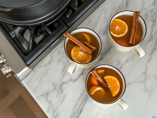 This image shows the final mulled cider served in a white mug, garnished with a cinnamon stick and an orange slice on top, ready for drinking.