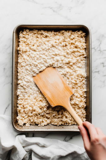 This image shows a lightly sprayed pan and spatula being used to press the mixture into the pan, flattening it with the back of the spatula.