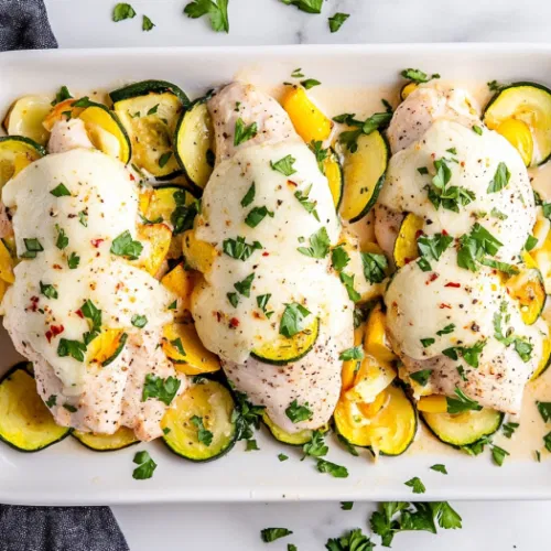 This image shows beautifully baked chicken breasts stuffed with vibrant slices of zucchini, yellow squash, red onion, and tomato, topped with melted mozzarella cheese, and garnished with fresh parsley.