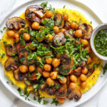 This image shows the completed dish of creamy polenta topped with sautéed mushrooms, microgreens, roasted chickpeas, and a drizzle of chimichurri, ready to be served.