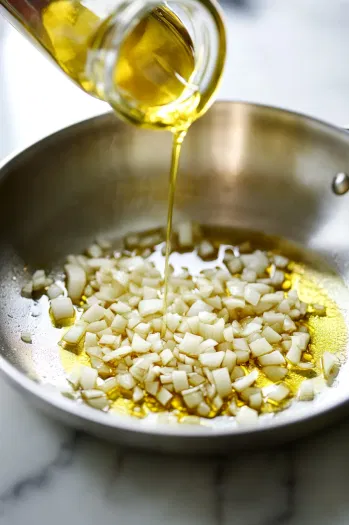 This image shows diced onion and garlic sizzling in olive oil in a skillet, becoming soft and fragrant to form the base of the sauce.