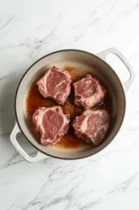 This image shows a pork shoulder being seared in a large Dutch oven with hot avocado oil, turning golden brown on all sides.