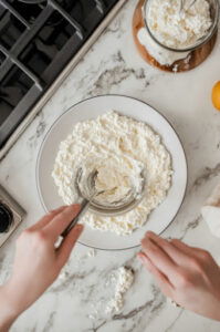 This image shows the back of a spoon being used to create a smooth surface with a small well in the center of the spicy cottage cheese dip in a white bowl.