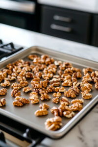 This image shows walnuts spread in a single layer on a baking sheet, toasting in the oven for about 5 minutes until they begin to brown.