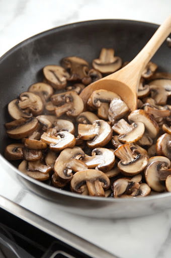 This image shows mushrooms being tossed in a pan with ½ teaspoon of salt and a few grinds of pepper, ensuring they are evenly coated.