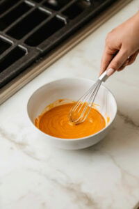 This image shows pumpkin puree, honey, melted coconut oil, and vanilla being whisked together in a small bowl until smooth.