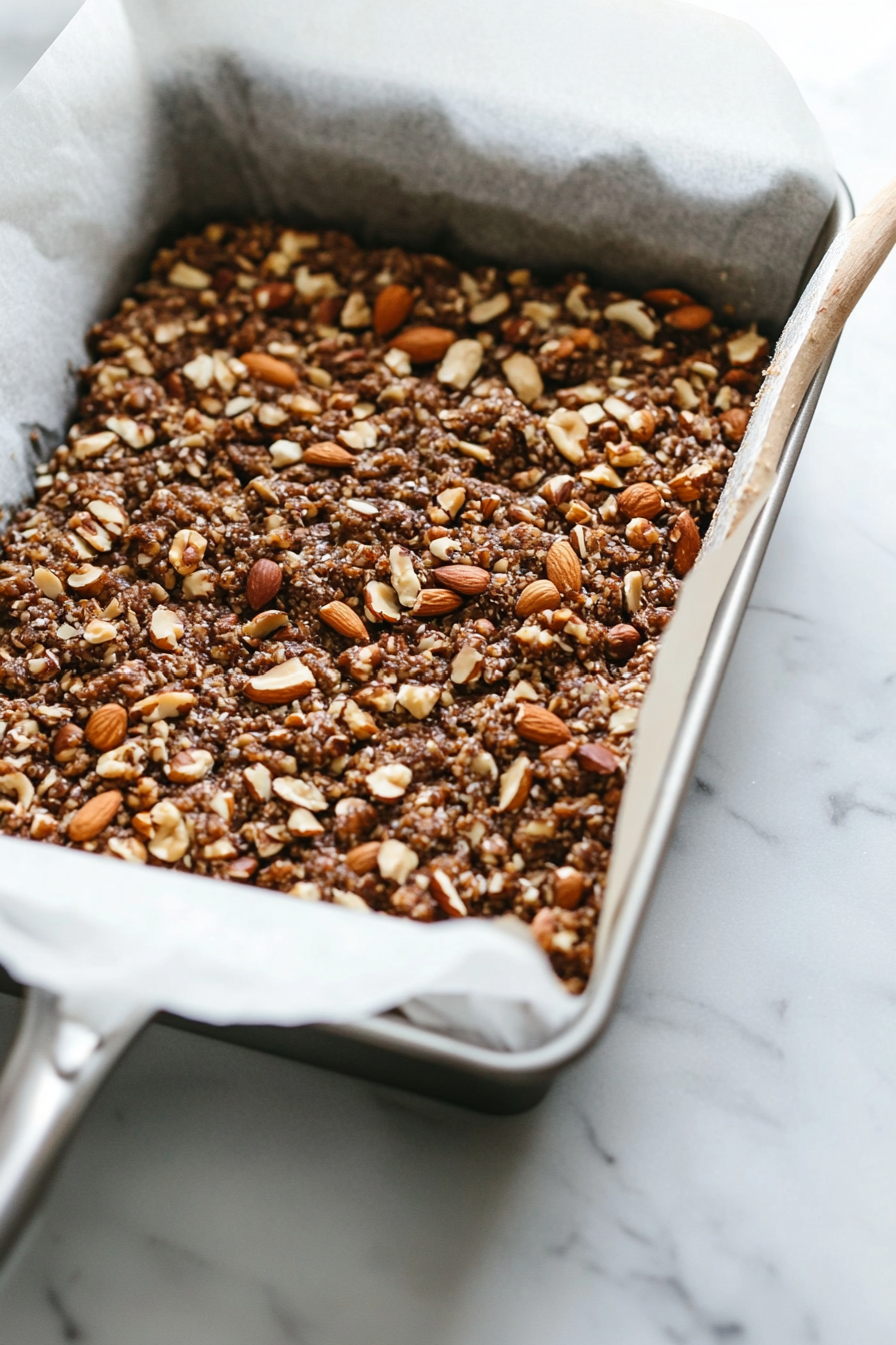 A bread pan lined with parchment paper on a white marble cooktop, with the nut roast mixture being firmly pressed into the pan with a spatula to ensure an even surface.