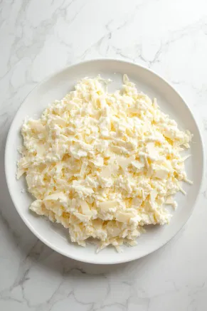 The whipped cream cheese mixture evenly spread over a serving platter, placed on the white marble cooktop, creating a creamy base layer.