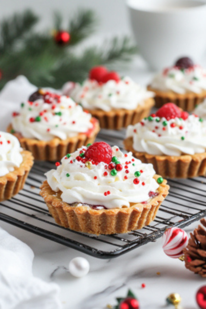 Completed Christmas dessert tarts on the white marble countertop, beautifully decorated with whipped cream, fruit, and festive sprinkles.