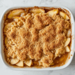 The freshly baked Apple Crisp rests on the white marble cooktop with steam rising, ready to be served.