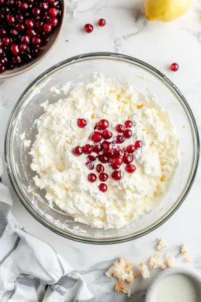 A large mixing bowl on the white marble cooktop with milk, lemon zest, vanilla extract, and dried currants stirred into the dry ingredients, forming a thick batter.