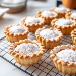 The baked pies are shown cooling on a wire rack over the white marble cooktop. A dusting of powdered sugar is added, and they are served warm with a side of cream or ice cream.