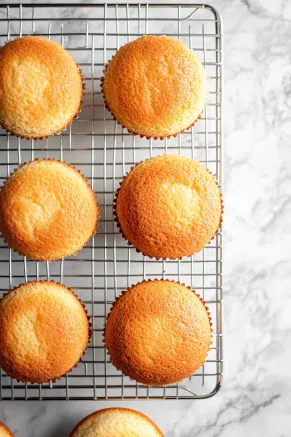 Baked cakes cooling on a wire rack placed on the white marble countertop, freshly removed from their pans.