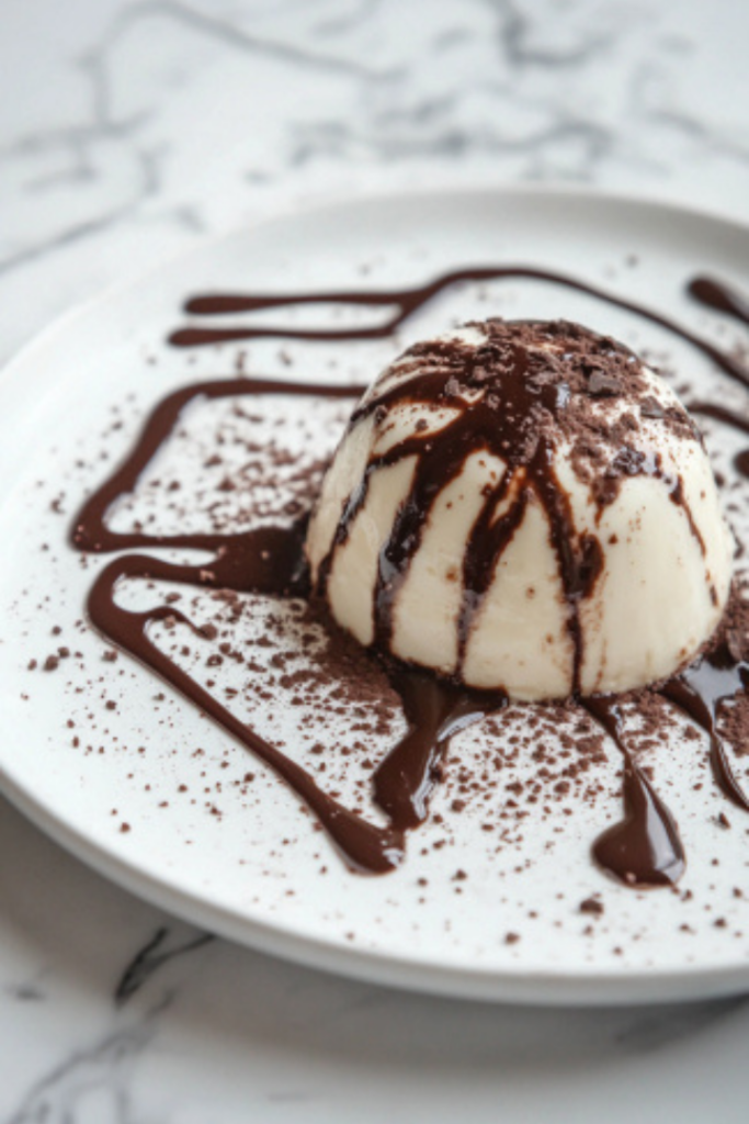 The panna cotta is shown unmolded onto a plate on the white marble cooktop, elegantly drizzled with the warm chocolate sauce, ready to be served chilled.