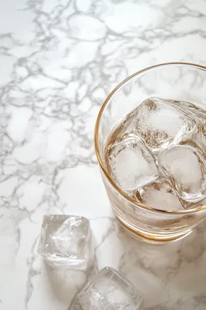 A glass filled with ice cubes on a white marble countertop, prepared to have the foamy coffee mixture poured in.